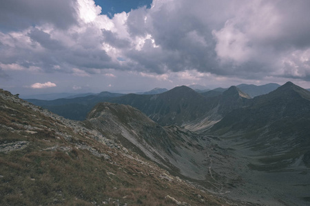 从斯洛伐克塔特拉山上的班尼科夫峰顶的山景全景，岩石景观和徒步旅行者的影子在明亮的一天，风暴云在阴天接近，老式的老电影看起来。