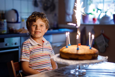 可爱快乐金发碧眼的小小孩男孩庆祝他的生日。在自制烤好的蛋糕，室内吹蜡烛的孩子。生日派对学校儿童家庭庆祝 6 年