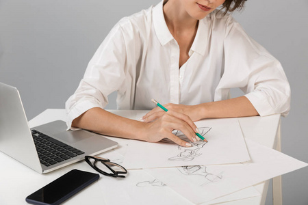 裁剪照片的年轻商务女性设计师孤立在灰色的墙壁背景上，坐在餐桌上的图纸。