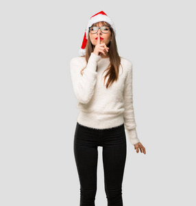 庆祝圣诞节的女孩，在灰色的背景下，用手指放在嘴里，表现出一种沉默的姿态