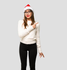 庆祝圣诞节的女孩用手指指着旁边，在孤立的灰色背景上展示一种产品