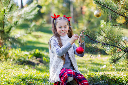 可爱的女孩在假期前在院子里户外装饰圣诞树。 圣诞快乐，节日快乐。