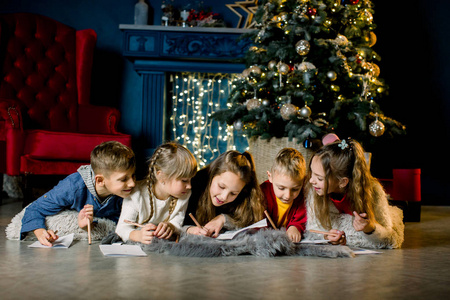 在节日前夕，可爱的小孩子在圣诞树的背景下给圣诞老人写了一封信