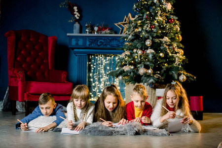 一群年幼的孩子躺在圣诞树背景上温暖的毛毯上，给圣诞老人写封信
