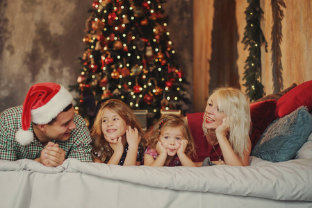 圣诞快乐，节日快乐 快乐的父母和两个小孩在客厅的床上一起在圣诞树附近玩耍