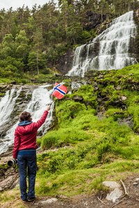 挪威山区强大的瀑布中挪威国旗的游客妇女。 国家旅游路线。