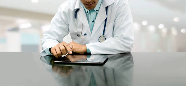 男医生坐在医院办公室的桌子上，拿着平板电脑。 医疗保健人员和医生服务。
