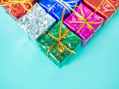 小彩色礼品盒在浅海蓝色背景与复制空间。 顶部的许多礼物包裹着五颜六色的闪亮的纸。