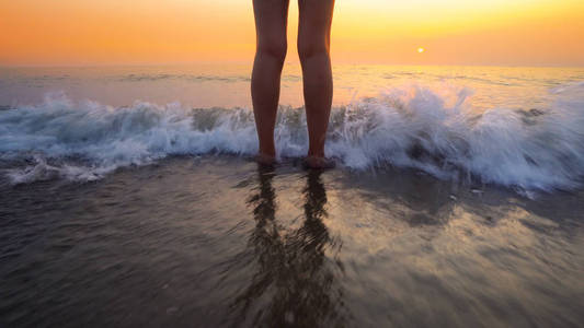 女人的脚溅在海滩日落的海浪上。 平静宁静放松的海洋水溅在美丽的海滩上