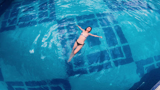 游泳池水上漂浮的年轻女子的鸟瞰图