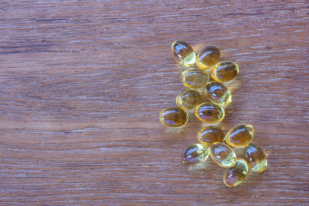 欧米茄3鱼肝油胶囊在木制背景上。 一堆大的金色半透明药丸在小玻璃碗里。 健康每天脂肪酸营养补充。 俯视图平面布局复制空间