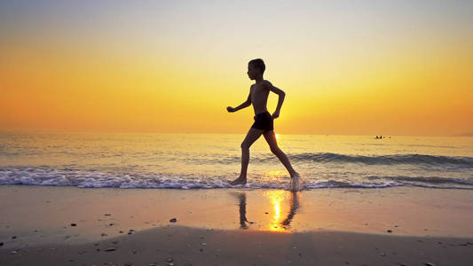 运动男孩在海边沙滩，背景是日落