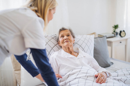 一位健康游客在与躺在家里床上的一名生病的老年妇女交谈