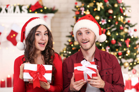 幸福的年轻夫妇带着礼品盒坐在家中圣诞树旁
