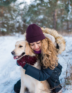 在雪地里抱着金毛猎犬狗的美丽的女人