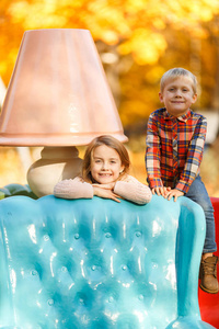 在秋天的公园里, 幸福的兄妹坐在蓝色的椅子上的照片