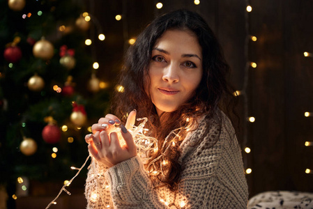 年轻女孩穿着白色杉树的圣诞灯和装饰，在黑暗的木制背景下寒假的概念