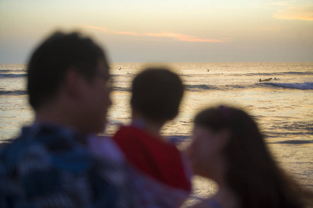 年轻快乐美丽的亚洲夫妇在浪漫的假日家庭旅行中，抱着小女儿一起欣赏日落海滩，看着大海，模糊的剪影。