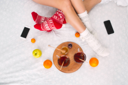 软照片的女人和男人在床上与手机和水果, 顶部的观点点。穿着温暖羊毛袜子的女性和男性腿