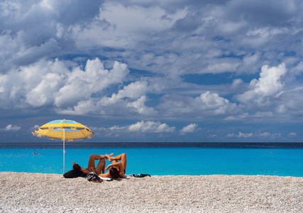 在希腊凯法洛尼亚岛上的爱奥尼亚海，阳光明媚的一天，游客在海滩伞下和美丽的海滩上喝着清澈的绿松石水。