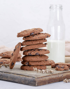 在一瓶牛奶后面的一块棕色木板上放着一叠圆形巧克力饼干