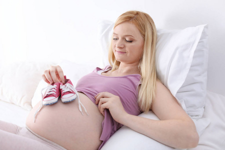 在光线充足的房间里，美丽的孕妇在肚子附近抱着婴儿奶