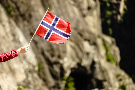 游客手拿挪威国旗在岩石石山背景。