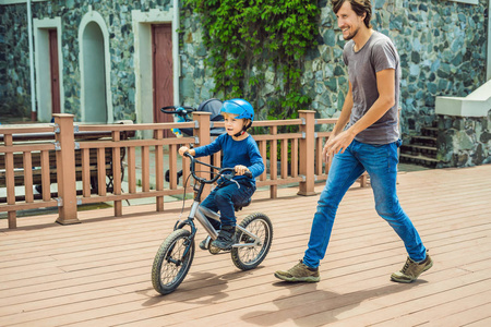 父亲在公园里帮助小儿子骑自行车。