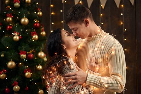年轻夫妇在圣诞节装饰和灯光杉树上深色的木制背景新年假期概念