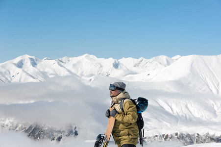一个人站在山上，手里拿着棕色的滑雪板，在佐治亚州著名的旅游胜地眺望远方