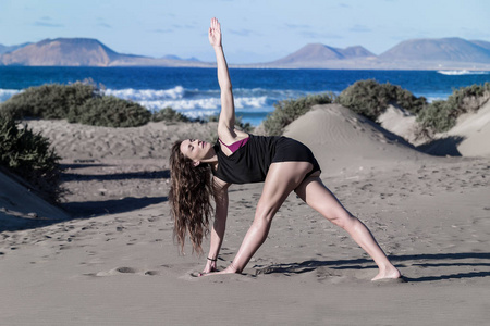 年轻苗条的女人，长发在沙滩上训练瑜伽体式，阳光明媚