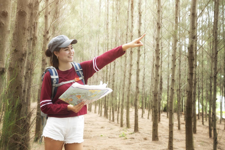 时髦的游客持有和看地图的旅行生活方式概念冒险旅行者与背包背景森林景观地平线年轻女孩徒步旅行者指向徒步旅行计划。
