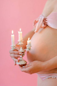 特写镜头孕妇在内衣抱着肚子和保持蜡烛