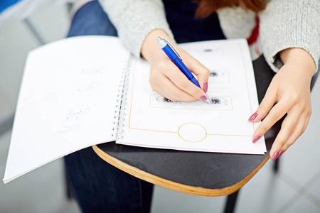 妇女在笔记本上写字, 坐在学生桌上