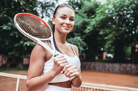 对胜利有信心。 运动中美丽的年轻女子戴着网球拍，看上去很高兴。