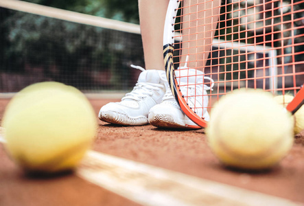 运动女孩的腿靠近网球拍和球。 网球场上儿童腿的裁剪图像。