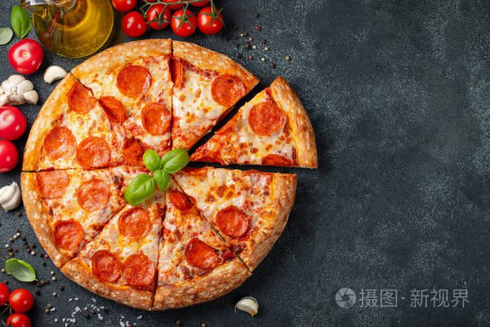 美味的意大利香肠比萨饼和烹饪原料番茄罗勒在黑色混凝土背景.