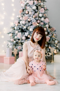 圣诞快乐，节日快乐 快乐的妈妈和她可爱的女儿坐在地板上玩得很开心，在室内圣诞树附近一起玩。