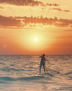 日落时，漂浮在海上的年轻人站起来，划着船板。