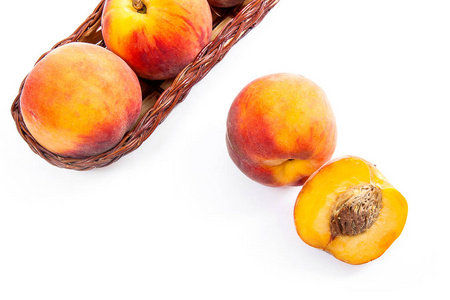 黄色木篮中的几个全甜多汁的桃子水果，整个水果和篮子前的一半桃子孤立在白色的背上