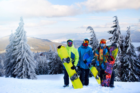 三个滑雪者在滑雪场摆姿势。朋友们带着滑雪板爬到山顶, 穿过森林, 穿着反光护目镜, 穿着五颜六色的时尚服装