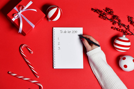 女性手工书写的最高视野在新的一年2019年在空白笔记本与礼品盒和党装饰在红色背景