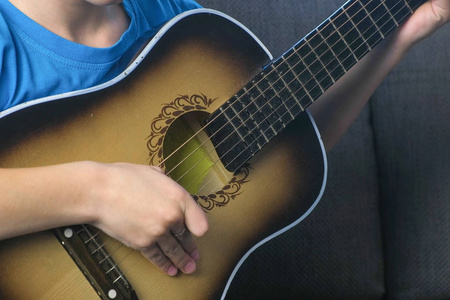 男孩坐在沙发上弹吉他, 双手特写。学习演奏乐器的概念