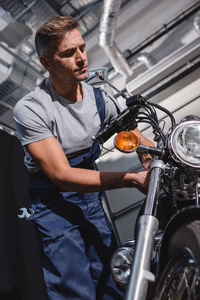 穿着工作服的英俊的成年机械师在车库里修理摩托车
