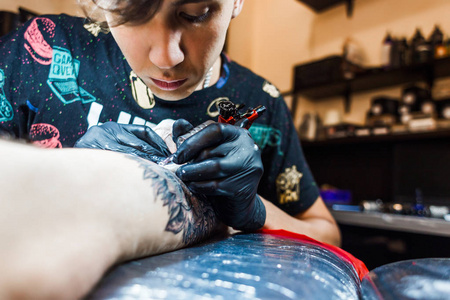 纹身艺术家在一个人的身体上创造了一幅画。纹身机和手的特写