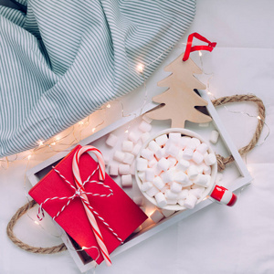 新年或圣诞广场，平躺，顶部视图与热可可咖啡巧克力与棉花糖杯圣诞节庆祝红色礼物盒在木制托盘在床上与灯。 博客社交媒体2019