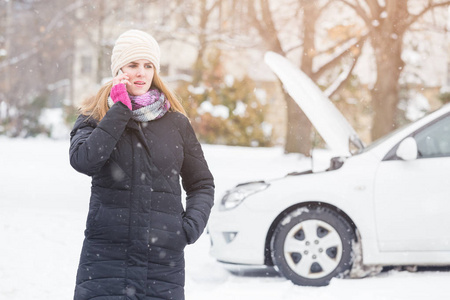 年轻的女人用智能手机打电话给道路援助。 冬季和车辆概念。
