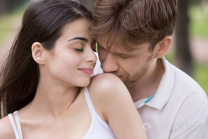 爱的男人亲吻妇女肩膀与柔情在公园