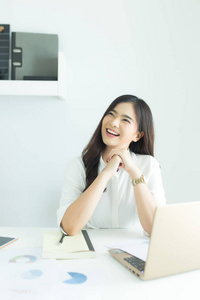年轻的亚洲商界女性微笑着，思考着现代办公室办公桌上的工作。