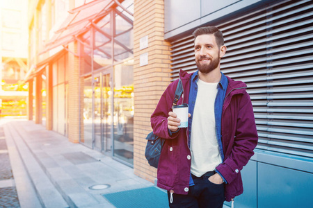 英俊的年轻人穿着紫色的冬衣喝咖啡。那个在街上喝咖啡的家伙太阳耀斑